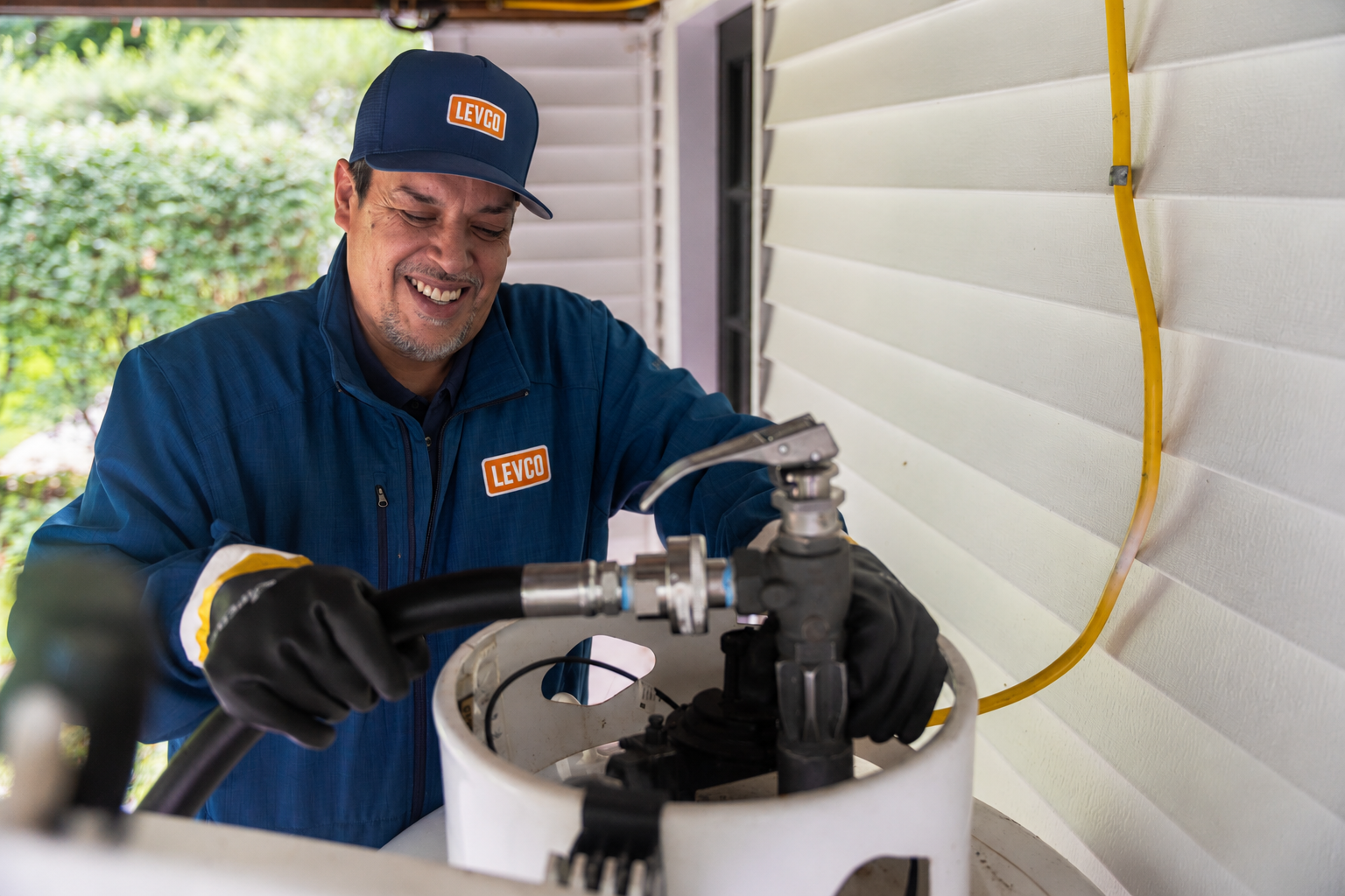 Levco technician connecting a delivery hose to a residential propane tank beside a Connecticut home