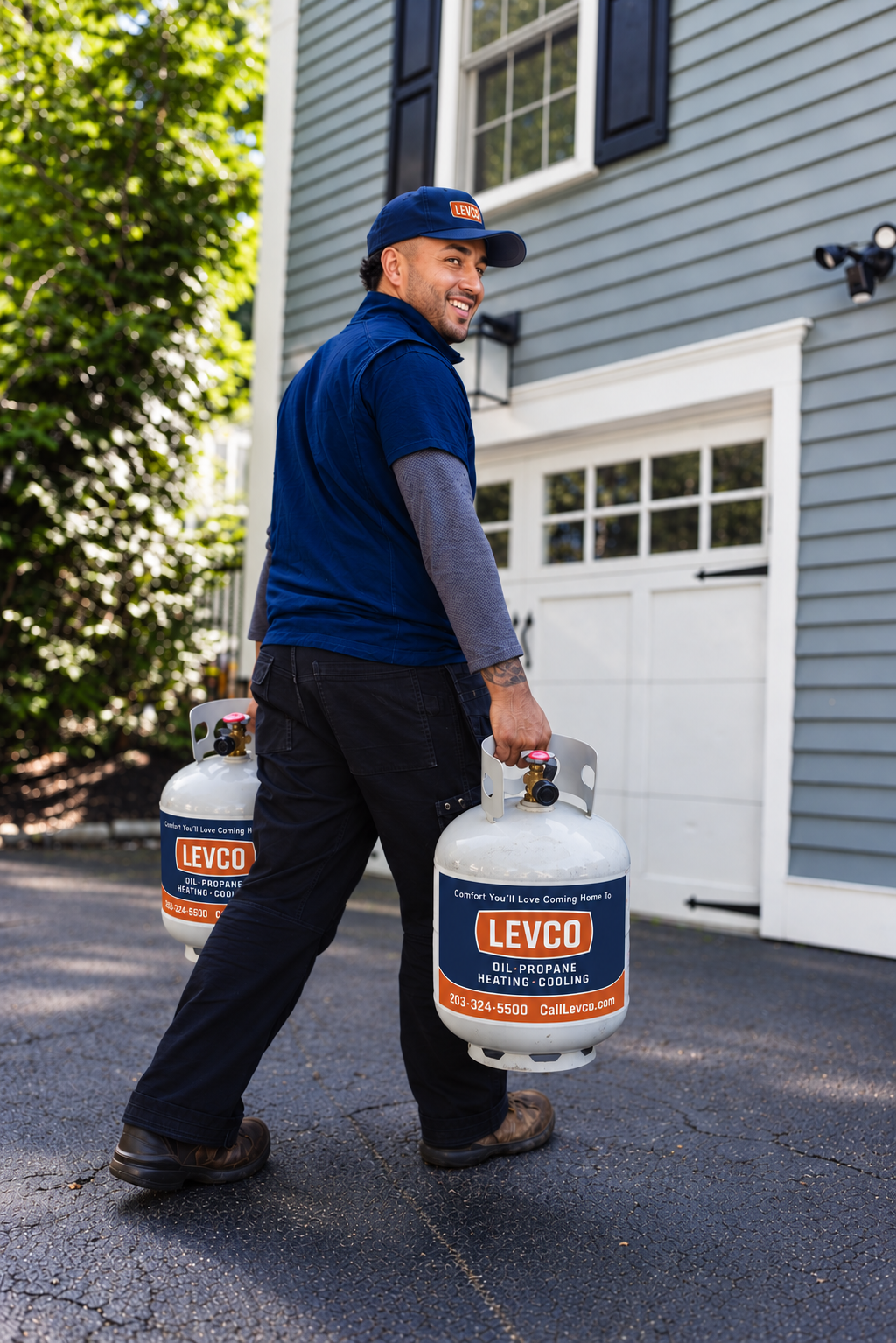 Levco driver carrying two Levco-branded 20-lb propane cylinders across a driveway