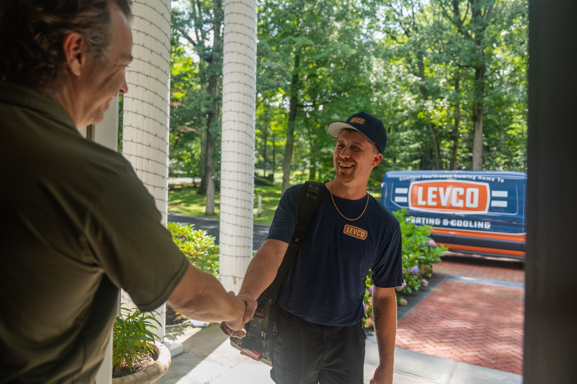 Levco technician shaking hands with a homeowner at the front door beside a Levco van