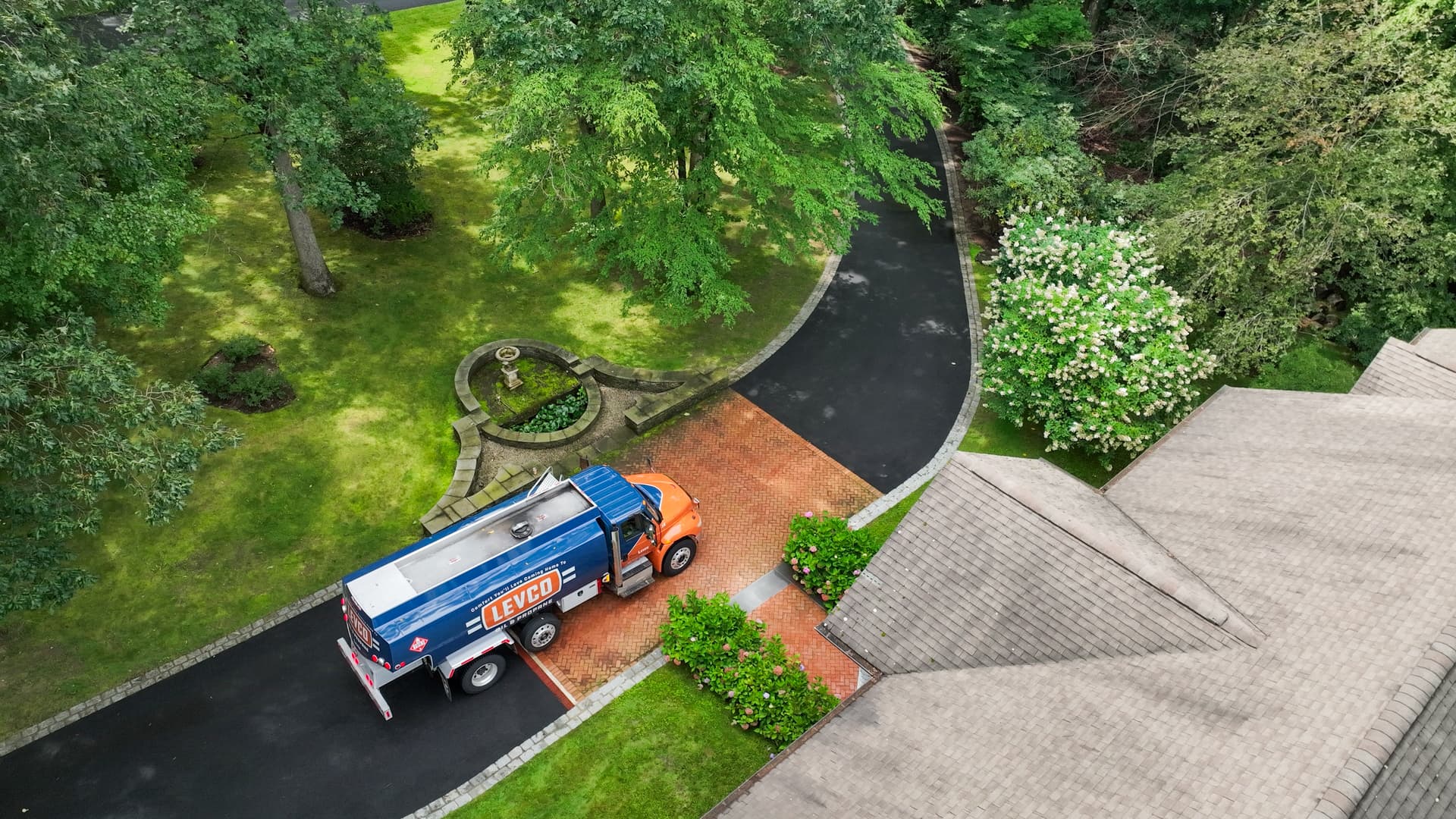 Aerial view of a Levco oil truck on a brick-inlay driveway beside a fountain and hydrangeas