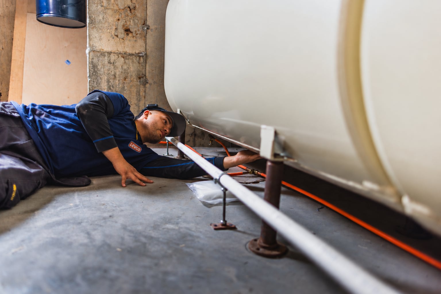 Levco technician installing and checking the piping beneath an indoor heating oil tank